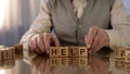 Senior man making word help of wooden cubes on table, parkinson disease, tremor