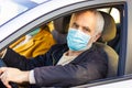 Senior man in a medical face mask driving a car. Coronavirus pandemic concept. Road trip, travel and old people concept - happy se