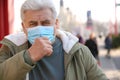 Senior man with medical mask coughing on street. Virus protection