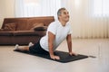 Senior man meditating while doing cobra pose in living room. Stretching exercises. Indoor shot of happy man practicing