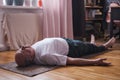 Senior man meditating on a wooden floor and lying in Shavasana pose.