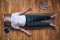 Senior man meditating on a wooden floor and lying in Shavasana pose.