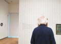 Senior man observing artwork in museum room.