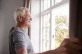 Senior Man Opening Bedroom Curtains And Looking Out Of Window