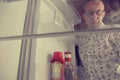 Senior man opening a refrigerator with little food. Selective focus. Hungry man looking for a late night meal in an