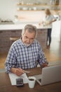 Senior man paying bills online on laptop in kitchen Royalty Free Stock Photo