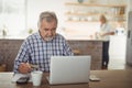 Senior man paying bills online on laptop in kitchen Royalty Free Stock Photo