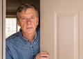 Senior man peering through front door for visitors during quarantine