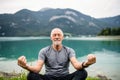 A senior man pensioner sitting by lake in nature, doing yoga exercise. Royalty Free Stock Photo