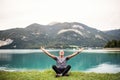 A senior man pensioner sitting by lake in nature, doing yoga exercise.