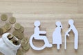 Senior man and people on wheelchairs with pregnant woman with stack of coins money on wooden background, Save money for