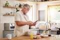 Senior man on a phone for cooking recipe, making breakfast in kitchen at home. Retirement, hobby and chef skill for old Royalty Free Stock Photo
