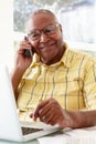 Senior Man On Phone Using Laptop At Home Royalty Free Stock Photo