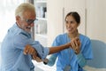 Senior man physiotherapy exercises with Asian woman caregiver or nurse physiotherapist in uniform helping aged male patient at Royalty Free Stock Photo