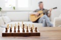 Senior man playing guitar in a bright living room with chessboard in the foreground Royalty Free Stock Photo