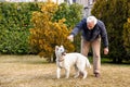 Senior man playing with White Swiss Shepherd puppy in the garden Royalty Free Stock Photo