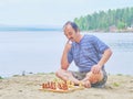 Senior man pondering a move in a game of chess and sitting on the beach near the lake