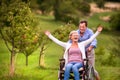 Senior man pushing woman in wheelchair, green autumn nature