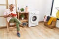 Senior man reading book waiting for washing machine at laundry room