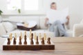 Senior man reading newspaper on a couch in a bright living room with chessboard in the foreground Royalty Free Stock Photo