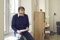 Senior man reading some letters and documents while sitting on windowsill at home