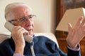 Unhappy Senior Man Receiving Unwanted Telephone Call At Home