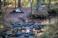 Senior man reclines on bench by hiking trail in woods by stream Royalty Free Stock Photo