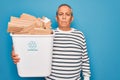 Senior man recycling holding trash can with cardboard to recycle over blue background with a confident expression on smart face Royalty Free Stock Photo