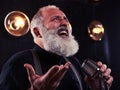 Senior man rejoices while singing in the vintage silver microphone isolated in studio Royalty Free Stock Photo