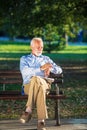 Senior man relaxing in park on a sunny day seated on a wooden bench and waiting for someone Royalty Free Stock Photo