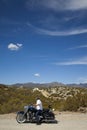 Senior man riding motorcycle on desert road looking to mountains in background