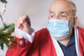 senior man in Santa Claus suit wearing a face mask and putting ornaments on Christmas tree Royalty Free Stock Photo