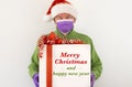 A senior man with santa hat wearing surgical mask and protective gloves due to coronavirus pandemic. Holding a Christmas gift box Royalty Free Stock Photo