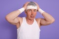 Senior man scratching his head in confusion, wearing white sleeveless t shirt, touching his head, poses isolated over lilac Royalty Free Stock Photo