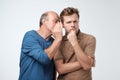 Senior man sharing secret or whispering gossips into his son ear. Telling family secret concept Royalty Free Stock Photo