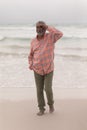 Senior man with shielding eyes and hand in pocket walking on the beach