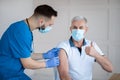 Senior man showing thumb up gesture while being immunized against coronavirus at hospital during his visit to doctor