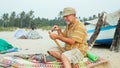 Senior man sits on the beach and making flute by hands