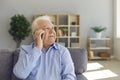 Senior man sits on a sofa in a bright living room and talks on the phone with a thoughtful look up. Royalty Free Stock Photo