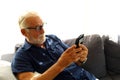 Senior man sitting alone and playing mobile phone at home.