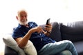 Senior man sitting alone and playing mobile phone at home.