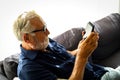 Senior man sitting alone for relaxation and playing game on smart phone in home Royalty Free Stock Photo