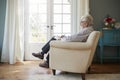 Senior man sitting in an armchair doing crossword, side view