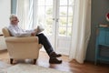 Senior man sitting in an armchair reading newspaper at home Royalty Free Stock Photo