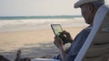 Senior man sitting on chairs enjoying time on beach travel vacation using tablet computer Royalty Free Stock Photo