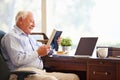 Senior Man Sitting At Desk Looking At Photo Frame