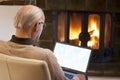 Senior man sitting by a fireplace and working with laptop Royalty Free Stock Photo