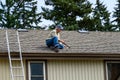 Senior man sitting on a house roof with a hammer, ready to make repairs Royalty Free Stock Photo