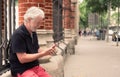 Senior man sitting outdoors in city street using mobile phone, elderly retired smiles Royalty Free Stock Photo