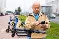 Senior man with smartphone activating electric scooter